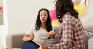 Mor bardaktan yudumlayan çeşitli bayan arkadaşlar evde kanepede parti balonlarıyla pasta paylaşıyorlar. Kutlama, dostluk, neşe, gündelik, rahat, canlı, sosyalleşme