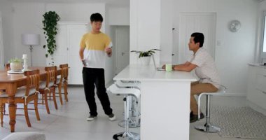 Asyalı adam kanepede oturmuş, evdeki belgeleri okuyor, odaklanmış ve rahatlamış görünüyor. İş, yaşam tarzı, gündelik, evrak, konsantrasyon, uzaktan çalışma