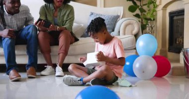 Mutlu siyah çift ve çok ırklı oğulları doğum günü hediyelerini açıyorlar, çocuğun doğum gününü evde kutluyorlar. Doğum günü, kutlama, parti, aile, çocukluk, ev hayatı ve ilişki kavramı.