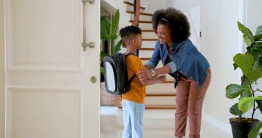 Mutlu siyahi anne, evdeki koridorda okula gitmeden önce çok ırklı oğluyla konuşuyor ve onu kucaklıyor. Eğitim, okul, aile, çocukluk, ev hayatı ve ilişki kavramı.