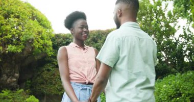 Afro-Amerikalı bir adam bahçede kadınlara sürpriz yapmayı teklif ediyor, ikisi de neşeyle gülümsüyor. Teklif, nişan, romantizm, aşk, kutlama, mutluluk
