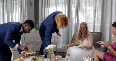 Mutlu gelin, damat ve arkadaşları oturma odasındaki düğün resepsiyonunda yemek yiyorlar. Kutlama, düğün, ilişki, parti ve arkadaşlık kavramı.