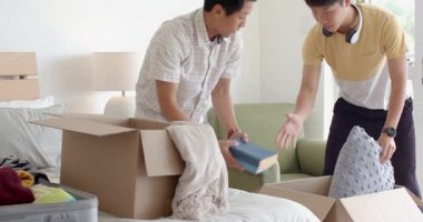 Evdeki yatakta giysileri ve resim çerçevesini karton kutuya koyan bir adam. Taşınma, taşıma, düzenleme, değişim, geçiş, hazırlık