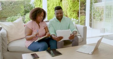 Laptop ve tablet kullanarak, evde dokümanları birlikte inceleyen olgun bir çift. Planlama, finans, takım çalışması, dijital cihazlar, yerli, işbirliği