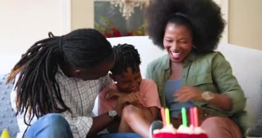 Mutlu siyah çift ve onların çok ırklı oğulları, erkek çocuğun doğum gününü evde kutluyorlar. Paketleri açan çocuk. Doğum günü, kutlama, parti, aile, çocukluk, ev hayatı ve ilişki kavramı.