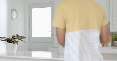 Modern mutfakta akıllı telefon ve dizüstü bilgisayar kullanan genç bir adam, verimli bir şekilde birden fazla iş yapıyor. Teknoloji, verimlilik, çalışma alanı, iletişim, yaşam tarzı, bağlantı