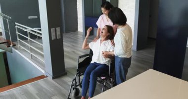 Tekerlekli sandalyede oturan mutlu son sınıf öğrencisi kadın hemşire ve bayan arkadaşıyla koridorda konuşuyor. üst düzey yaşam tarzı, engellilik, sağlık ve arkadaşlık konsepti.