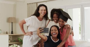 Çeşitli bayan arkadaşlar mezuniyeti şapkalı ve akıllı telefondan selfie çekerek kutluyorlar. Yoldaşlık, başarı, şenlik, yaşam tarzı, neşe, arkadaşlık, kutlama