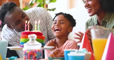Mutlu siyahi çift ve onların çok ırklı oğlu, çocuğun doğum gününü evde kutluyor, çocuk pastaya mum üflüyor. Doğum günü, kutlama, parti, aile, çocukluk, ev hayatı ve ilişki kavramı.