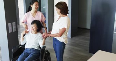 Tekerlekli sandalyede oturan mutlu son sınıf öğrencisi kadın hemşire ve bayan arkadaşıyla koridorda konuşuyor. üst düzey yaşam tarzı, engellilik, sağlık ve arkadaşlık konsepti.