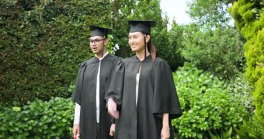 Açık havadan mezun olan kep ve cüppeli genç bir çift neşeyle gülümsüyor. Mezuniyet, kutlama, eğitim, başarı, mutluluk, üniversite