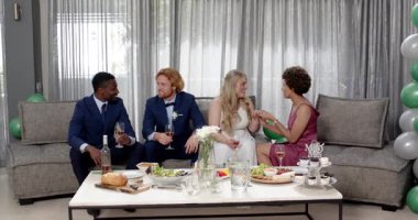 Mutlu gelin, damat ve arkadaşları oturma odasındaki düğün resepsiyonunda kadeh kaldırıyor. Kutlama, düğün, ilişki, parti ve arkadaşlık kavramı.