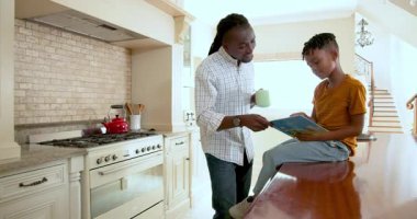 Mutlu siyah baba ve çok ırklı oğlu mutfakta birlikte kitap okuyorlar, çocuk evde mutfak atölyesinde oturuyor. Eğitim, okul, aile, çocukluk, ev hayatı ve ilişki kavramı.