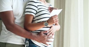 Çift oturma odasının penceresinde ultrason çıktısını fark ediyor hamileliği kutlayan şişkinliği kucaklıyor. Romantizm, samimiyet, aile, annelik, neşe, şefkat, bağ