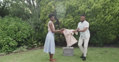 Genç çift çimenlere battaniye seriyor, birlikte pikniğe hazırlanıyorlar. Doğa, yaz, eğlence, eğlence, açık hava.