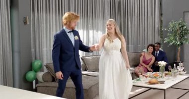 Mutlu gelin ve damat ve siyah dans ve çok ırklı erkek ve kadın arkadaşlar oturma odasında düğün resepsiyonunu izliyorlar. Kutlama, düğün, ilişki, parti ve arkadaşlık kavramı.