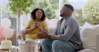 Afro-Amerikalı bir çift evde doğum günü kutluyor, pasta ve şampanyayla eğleniyorlar. Kutlama, mutluluk, birliktelik, kapalı alan, oturma odası