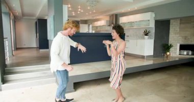 Mutlu ve çok kültürlü bir çift, gülümsüyor, kucaklaşıyor ve birlikte dans ediyorlar. Mutfağın yanında, oturma odasında. Taşınmak, konut ve ev hayatı kavramı.