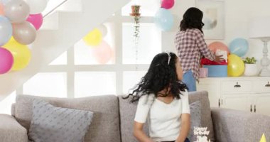 Çeşitli bayan arkadaşlar oturma odasındaki kanepede pasta ve balonlarla hediyelerini değiş tokuş ediyorlar. Doğum günü, kutlama, şenlik, kilometre taşı, toplanma, pastel, güneş ışığı