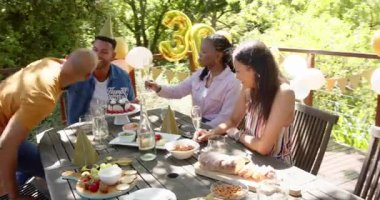 Güneşli bir günde, bahçedeki bir doğum günü partisinde hediyeleri açan bir grup mutlu çok ırklı ve siyah erkek ve kadın arkadaş. Kutlama, doğum günü, parti, yaz ve arkadaşlık kavramı.