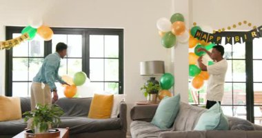 Bir grup mutlu, çok ırklı, beyaz ve Hintli erkek ve kadın arkadaş güneşli oturma odasında bir doğum günü partisi için dekorasyon hazırlıyorlar. Kutlama, doğum günü, parti, yaz ve arkadaşlık kavramı.