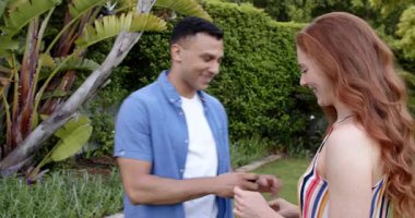 Mutlu adam diz çöküp, yüzük veriyor ve güneşli bahçede ortağına evlenme teklif ediyor. Nişan, aile hayatı, aşk, mutluluk, yaşam tarzı ve ilişki kavramı.