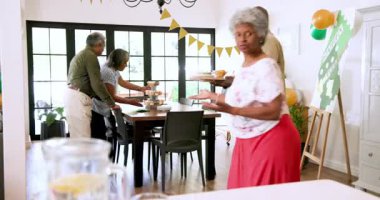 Bir grup mutlu üst düzey çok ırklı, beyaz ve siyah erkek ve kadın arkadaşlar oturma odasındaki emeklilik partisinde masa hazırlıyorlar. Kutlama, emeklilik, parti, son sınıf yaşam tarzı ve arkadaşlık kavramı.