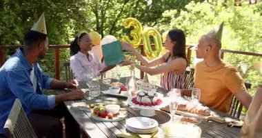 Güneşli bir günde, bahçedeki bir doğum günü partisinde hediyeleri açan bir grup mutlu çok ırklı ve siyah erkek ve kadın arkadaş. Kutlama, doğum günü, parti, yaz ve arkadaşlık kavramı.