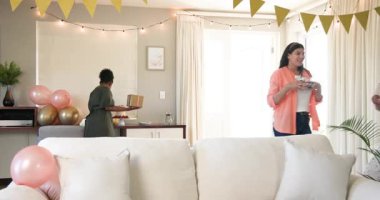 Üç mutlu çok ırklı ve siyah bayan arkadaş güneşli oturma odasındaki bir doğum günü partisinde masayı hazırlıyorlar. Kutlama, doğum günü, parti, yaz ve arkadaşlık kavramı.