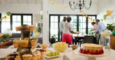 Bir grup mutlu üst düzey çok ırklı, beyaz ve siyah erkek ve kadın arkadaşlar oturma odasındaki bir doğum günü partisine hazırlanıyorlar. Kutlama, doğum günü, parti, son sınıf yaşam tarzı ve arkadaşlık konsepti.