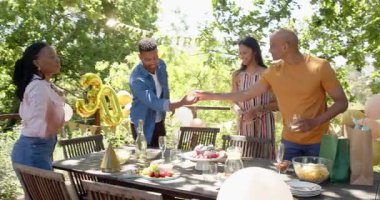 Bir grup mutlu çok ırklı ve siyah erkek ve kadın arkadaş güneşli bir günde bahçede bir doğum günü partisi için hazırlanıyorlar. Kutlama, doğum günü, parti, yaz ve arkadaşlık kavramı.