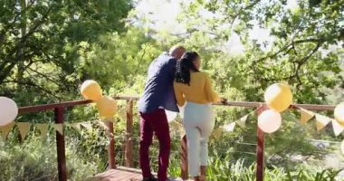 Mutlu çok ırklı ve siyah çift, güneşli bir günde balonlarla terasta evlenme teklif ediyor, kucaklıyor ve kutluyor. Kutlama, nişan, parti, yaz konsepti.