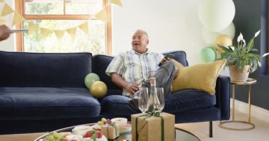 Mutlu kıdemli muhtelif adam balonlu odada siyah bir kadından mum eşliğinde doğum günü pastası alıyor. Kutlama, üst düzey yaşam, aşk, mutluluk, yaşam tarzı ve ilişki kavramı.