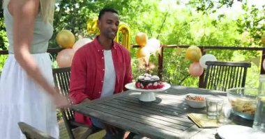 Mutlu siyah adam ve beyaz bayan partneri otuzuncu yaş gününü kutluyor, erkek bahçede doğum günü pastası yiyor. Parti, doğum günü, eğlence, eğlence, aşk, mutluluk, yaşam tarzı ve ilişki konsepti.