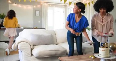 Güneşli oturma odasındaki bir doğum günü partisinde üç mutlu çok ırklı ve beyaz bayan arkadaş masasını temizliyor. Kutlama, doğum günü, parti, yaz ve arkadaşlık kavramı.