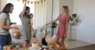 Bebek kucaklayan ve oturma odasındaki bir doğum günü partisinde kadeh kaldıran üç mutlu, çok ırklı ve beyaz bayan arkadaş. Kutlama, doğum günü, parti, yaz ve arkadaşlık kavramı.