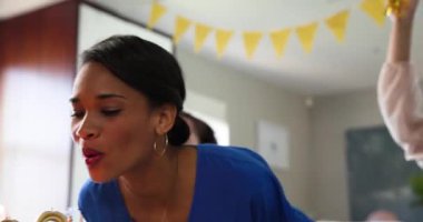 Üç mutlu çok ırklı ve beyaz bayan arkadaş güneşli oturma odasındaki bir doğum günü partisinde pastaya mum üflüyorlar. Kutlama, doğum günü, parti, yaz ve arkadaşlık kavramı.