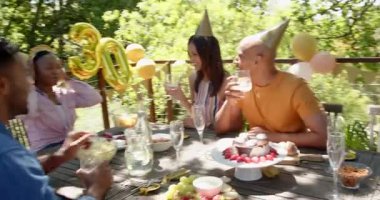 Bir grup mutlu çok ırklı ve siyah erkek ve kadın arkadaş güneşli bir günde bahçede bir doğum günü partisinde kadeh kaldırıyorlar. Kutlama, doğum günü, parti, yaz ve arkadaşlık kavramı.