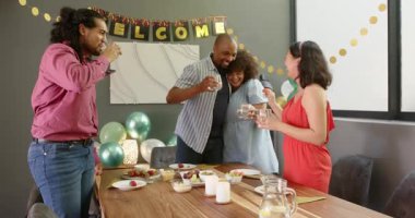 Bir grup mutlu, çok ırklı, siyah ve Çinli erkek ve kadın arkadaş masada oturmuş, oturma odasındaki yeni ev partisi için kadeh kaldırıyorlar. Kutlama, parti, yaz ve arkadaşlık konsepti.