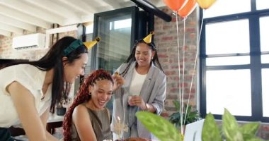 Üç farklı bayan meslektaşımız doğum gününü kutluyor ve ofiste pastaya mum üflüyorlar. Takım çalışması, doğum günü, iş ve iletişim konsepti.