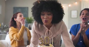 Üç mutlu çok ırklı ve beyaz bayan arkadaş güneşli oturma odasındaki bir doğum günü partisinde pastaya mum üflüyorlar. Kutlama, doğum günü, parti, yaz ve arkadaşlık kavramı.