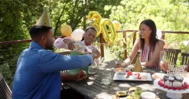 Bir grup mutlu çok ırklı ve siyah erkek ve kadın arkadaş güneşli bir günde bahçede bir doğum günü partisinde kadeh kaldırıyorlar. Kutlama, doğum günü, parti, yaz ve arkadaşlık kavramı.