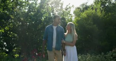 Mutlu siyah adam, beyaz kadın ortağına diz çöküp, güneşli bir bahçede nişan yüzüğü vermeyi teklif ediyor. Nişan, aşk, mutluluk, yaşam tarzı ve ilişki kavramı.