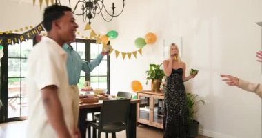 Bir grup mutlu, çok ırklı, beyaz ve Hintli erkek ve kadın arkadaş güneşli oturma odasında sarılıp kutluyorlar. Kutlama, doğum günü, parti, yaz ve arkadaşlık kavramı.