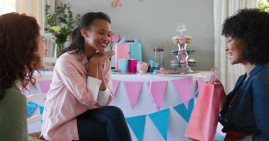 Üç mutlu çok ırklı ve beyaz bayan arkadaş güneşli oturma odasındaki bebek partisinde hediye veriyorlar. Kutlama, annelik, parti, yaz ve arkadaşlık kavramı.
