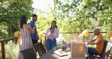 Bir grup mutlu çok ırklı ve siyah erkek ve kadın arkadaş güneşli bir günde bahçede bir doğum günü partisinde kutlama yapıp kucaklaşıyorlar. Kutlama, doğum günü, parti, yaz ve arkadaşlık kavramı.