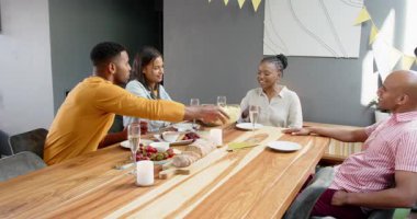 Bir grup mutlu çok ırklı ve siyah erkek ve kadın arkadaş masada oturmuş oturma odasındaki bir doğum günü partisinde kadeh kaldırıyorlar. Kutlama, doğum günü, parti, yaz ve arkadaşlık kavramı.