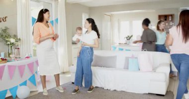 Bebekleri olan, çok ırklı, beyaz ve siyah bir grup arkadaş güneşli oturma odasındaki bir bebek partisinde temizlik ve sohbet yapıyorlar. Kutlama, annelik, parti, yaz ve arkadaşlık kavramı.