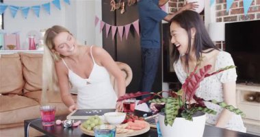 Bir grup mutlu arkadaş güneşli oturma odasında bebek partisi için dekorasyon hazırlıyor. Kutlama, annelik, parti, yaz ve arkadaşlık kavramı.