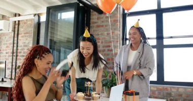Üç farklı bayan meslektaşımız doğum gününü kutluyor ve ofiste pastaya mum üflüyorlar. Takım çalışması, doğum günü, iş ve iletişim konsepti.